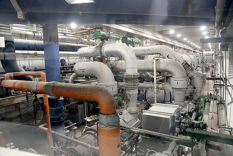 Several large curved pipes stretch ceiling to floor, connect to a room-size machine on the floor.