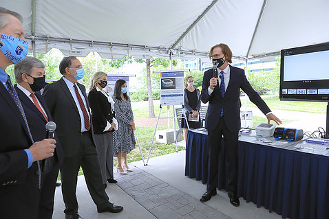 Tromberg stands in front of a display table and speaks to several senators under a tent