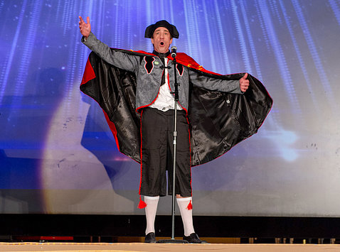 Austin sings on stage with outstretched arms holding out his black and red cape.