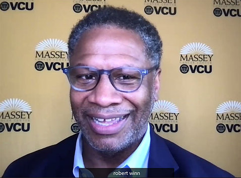 A smiling Winn speaks on videocast with VCU Massey logos as screen wallpaper behind him.