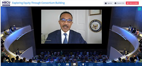 A screen shot of the conference room with circular seating and Rep. Kweisi Mfume showing on the large video screen.