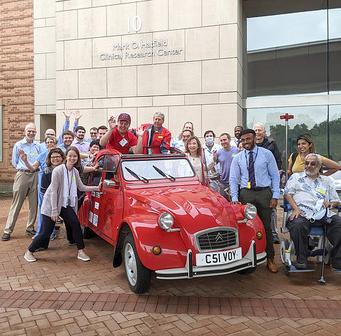 A group of health professionals stand around a red Volkswagen Beetle 