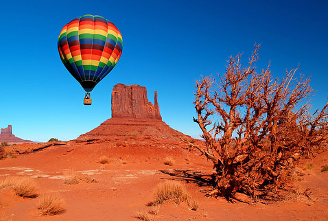 A colorful hot air balloon floats over red rock terrain with a bright blue sky, on Navajo land, 