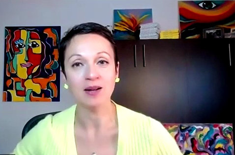 Kogan, speaking on video, sits in her office with colorful paintings on the wall behind her.