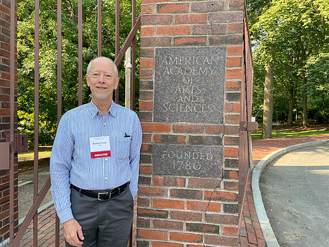 Youle standing outside by a brick wall with plaque reading: American Academy of Arts and Sciences, founded 1780"