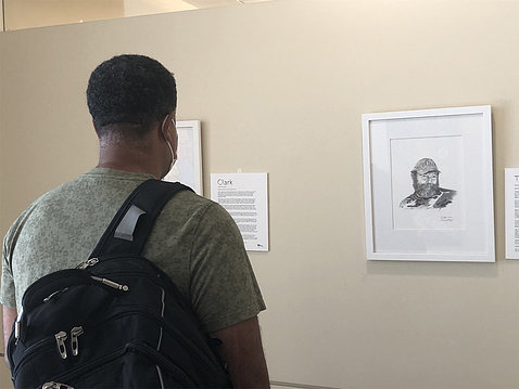 A man wearing a backpack reads a narrative on the wall next to portrait drawn by Clower. The exhibit is displayed on the main floor, east alcove, of the Clinical Center.
