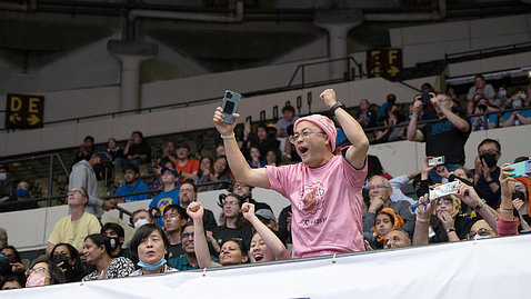 Man in pink T shirt and pink skullcap raises arms and yells 