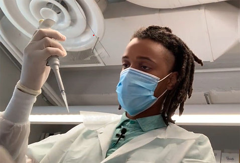 Screenshot of Preston in white lab coat and gloves, holding a pipetter in the lab