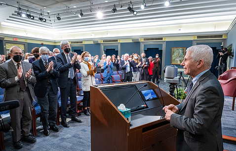 Fauci at podium faces standing attendees 