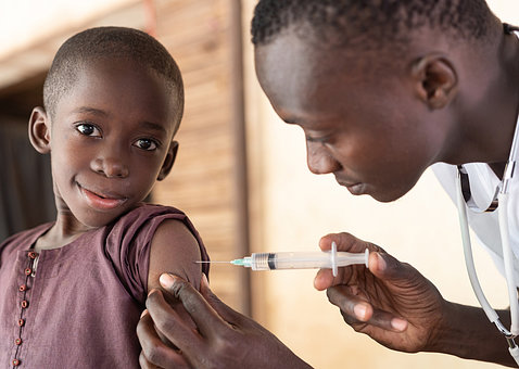 A young African boy puts on a brave face as a doctor inserts a needle into his arm