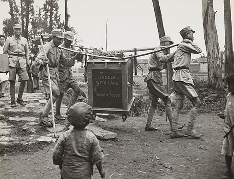 A black-and-white photo shows men in uniform carrying a large box filled with blood donations.