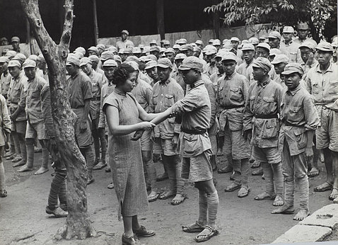 Wong inspects veins in arm of a soldier, as dozens of other soldiers stand nearby.
