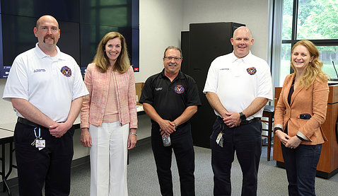 NIH leaders and firehouse leaders stand posing together in the station's classroom.