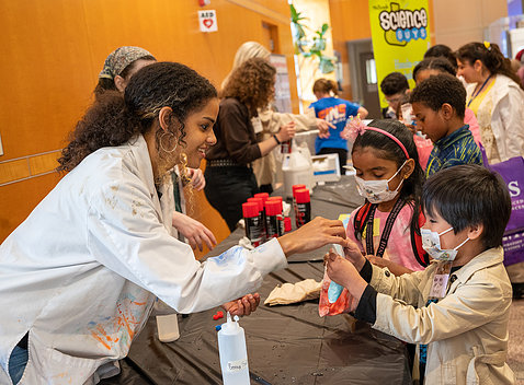 Scientist in white lab coat hands a bag of slime to kids.