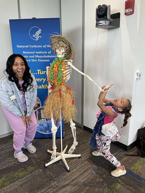 Mother and daughter pose with skeleton model wearing leis and grass skirt.