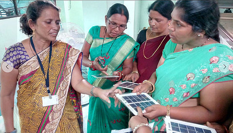 Three women examine small solar panels as a fourth woman looks on