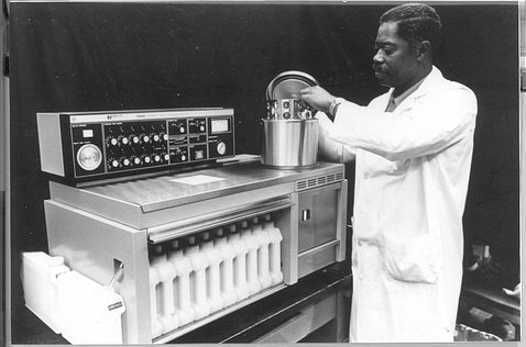 Charles Green, in white lab coat, putting samples into a tissue processor machine in the lab