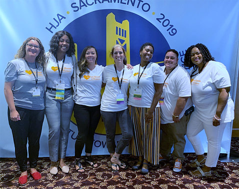 A group photo of colleagues at a conference with a HJA Sacramento banner behind them