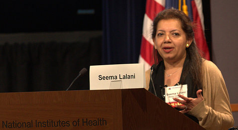 Lalani speaks behind a podium, which bears a card with her name on it.