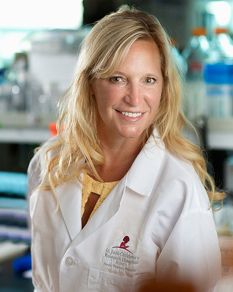 A smiling blond woman wearing a lab coat with a St. Jude's logo. 