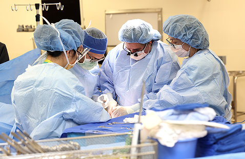 Four people in scrubs and face masks huddled over a surgical table
