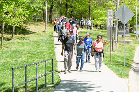 A group of people run together along the path by NIH's main campus, surrounded by grass and trees.