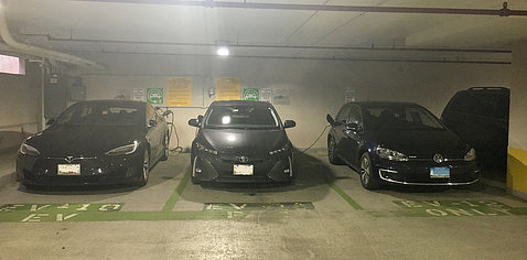 Three cars in garage in parking spots marked EV with electric chargers on wall