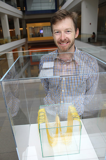 Conway smiles, standing behind one of his exhibit pieces enclosed in a clear glass case..