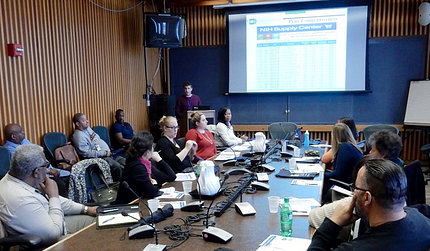 People seated around a conference table, looking at a slide screen