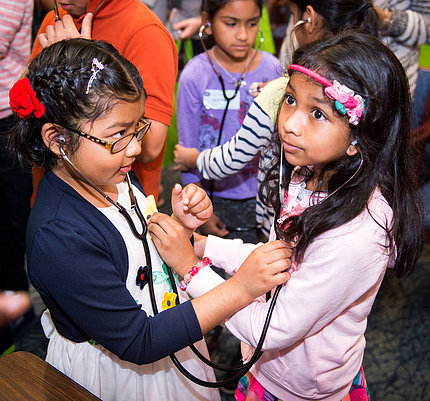 Two young girls listen to each other's heartbeat with stethoscopes