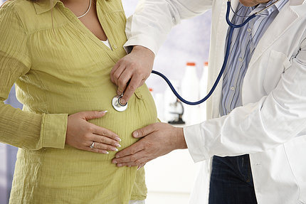 A doctor holds a stethoscope to a pregnant woman's belly