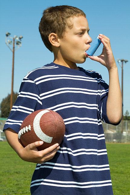 Boy using an asthma inhaler while holding a football outside.