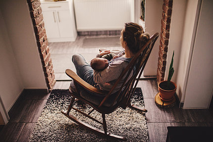 A woman holds a woman a baby while sitting in a rocking chair 