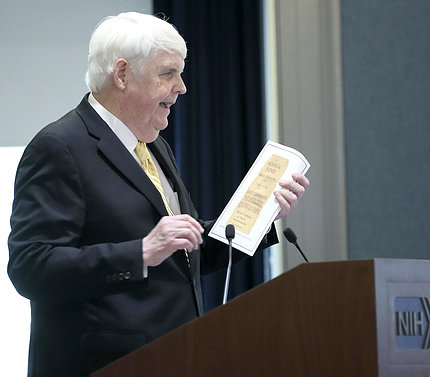 At the podium, Clifford holds up clipping of the want ad he answered to work at NIH.
