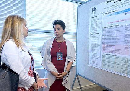 Two women talk in front of a scientific poster at the forum.