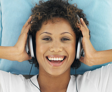 A smiling woman listens to music through headphones.