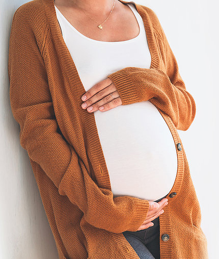 A pregnant woman cups her hands around her belly.