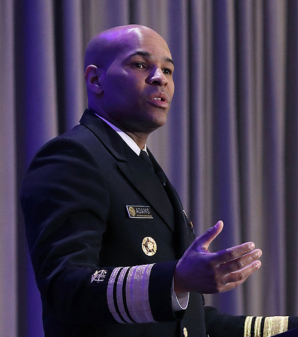 The surgeon general, with outstretched hand, speaks at podium.