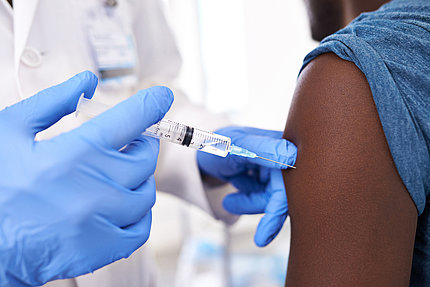 Close-up of injection with gloved hands holding syringe at exposed upper arm