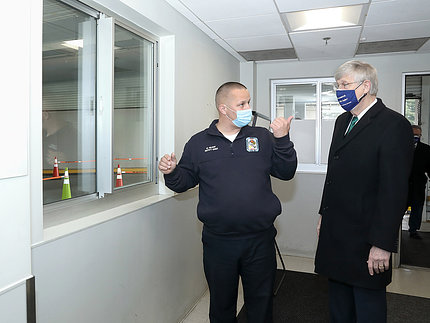 At a window in the facility, Gilroy points out features to Collins.