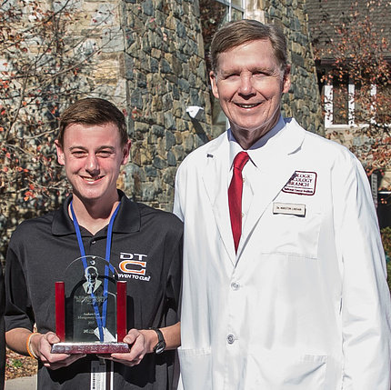 Andrew Lee, holding his William Donald Schaeffer Helping People Award, stands with Dr. Marston Linehan in front of the Children's Inn.