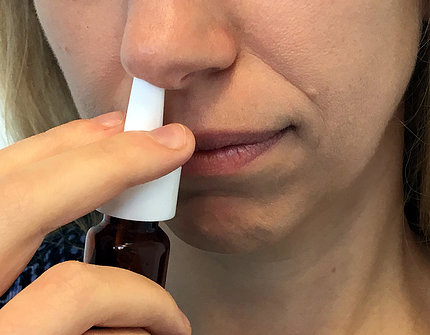 A woman holds a nasal spray bottle up to her nose.