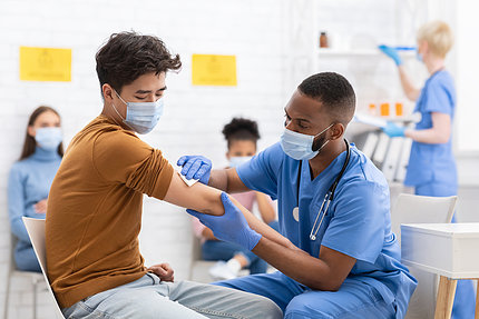 A nurse in scrubs disinfects a man's arm