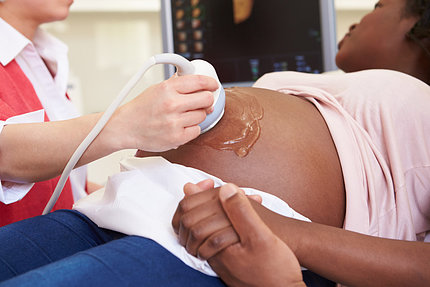 Pregnant black woman's belly being scanned with ultrasound instrument held by a white hand.