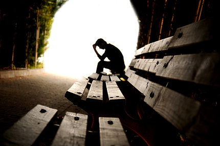 A silhouette of a person holds their head on a park bench