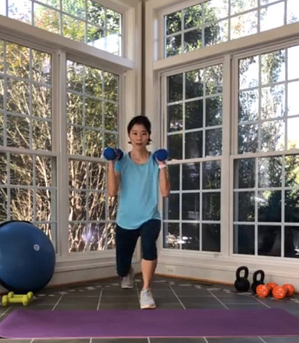 Ashley Choi holds blue weights and lunges on a purple mat in room with big windows during a virtual fitness class.