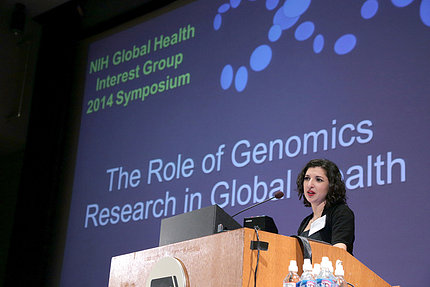 Taaffe speaks from NIH podium with seminar title slide projected on screen behind her