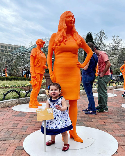 Toddler girl smiles widely in front of statue.