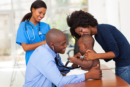 Black nurse, doctor, baby, and mom smile during checkup.