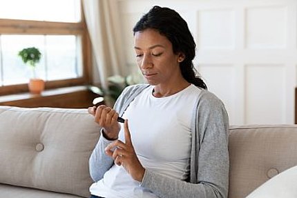 Woman of color seated on sofa uses fingerstick device